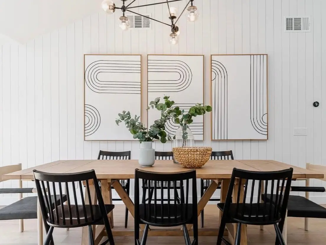 A modern farmhouse dining room featuring a light wood table, black spindle-back chairs, and large abstract wall art, showcasing modern farmhouse decor ideas.