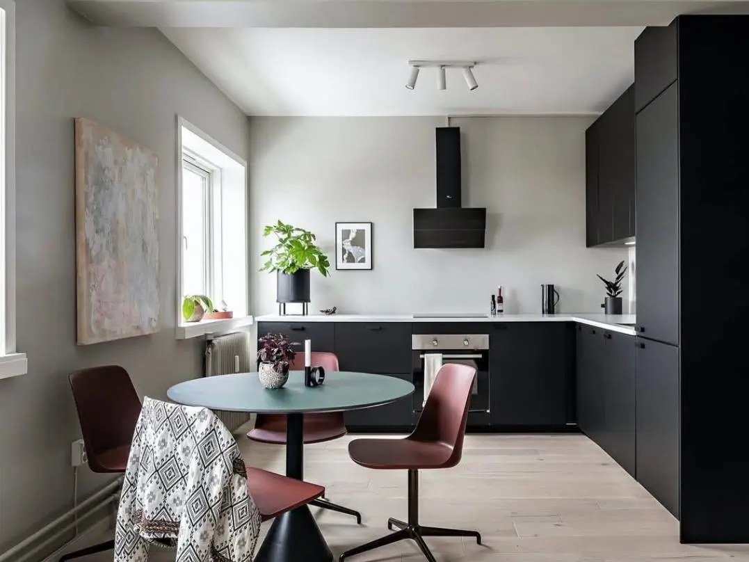 A modern open kitchen with sleek matte black cabinets and a round dining table with reddish-brown chairs in the foreground.