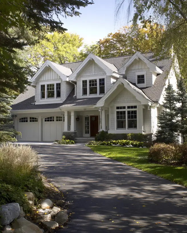 Large modern craftsman house with multiple gables, light gray siding, and an attached two-car garage set in a wooded landscape.
