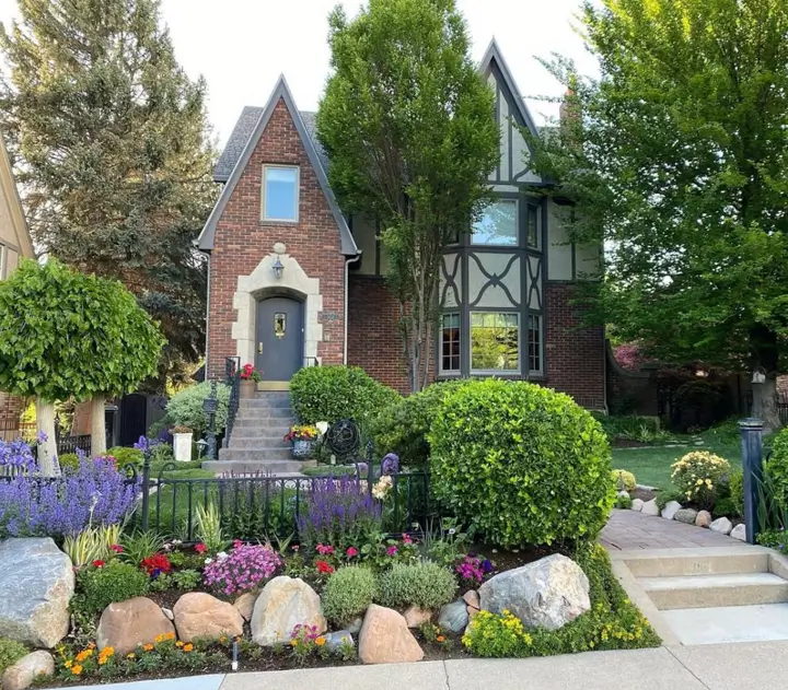 Charming small Tudor-style house with a red brick lower story, classic half-timbering, and a vibrant, layered front garden.