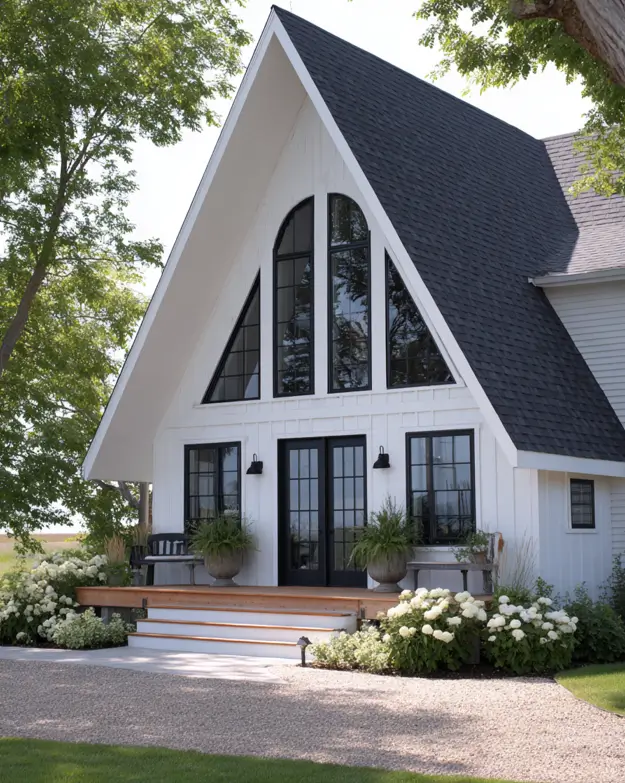 A modern farmhouse with a white A-frame gable, black arched windows, and a porch surrounded by hydrangeas.