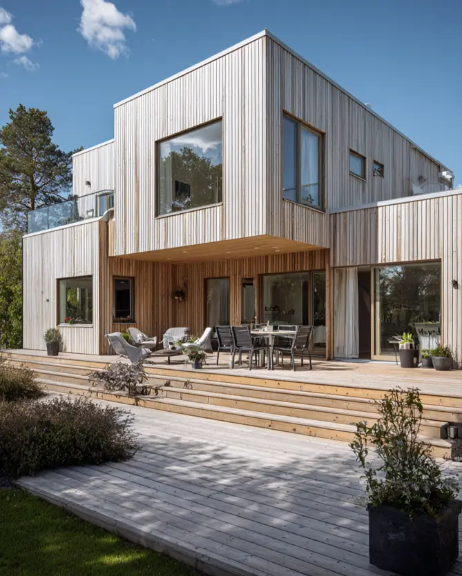 A modern Scandinavian house exterior with light wood siding and a large, multi-level wooden deck perfect for outdoor entertaining.