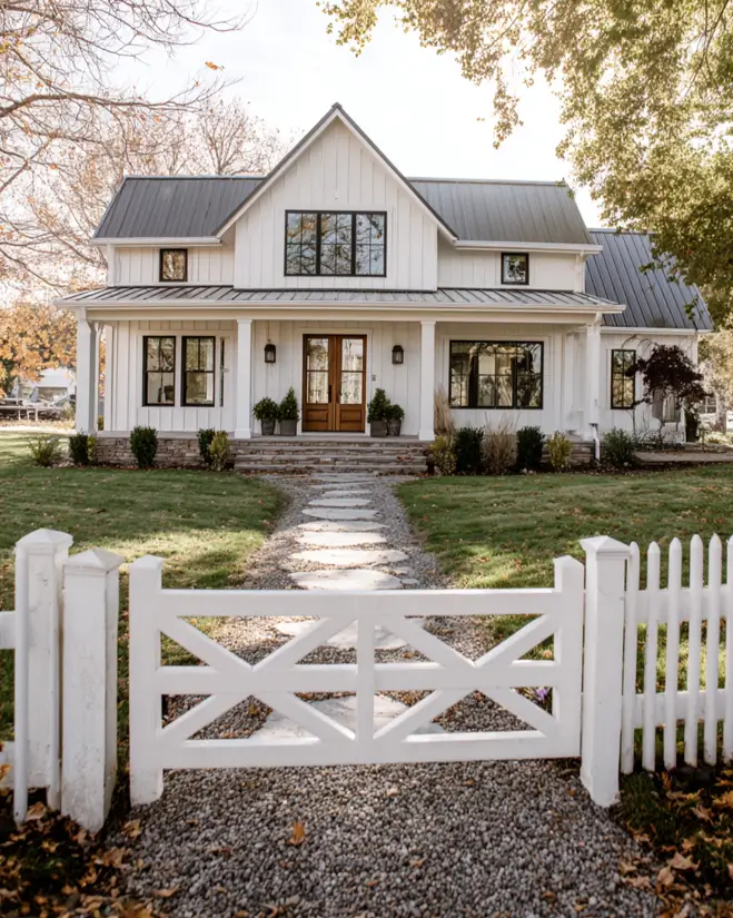 A welcoming white modern farmhouse with a stone path leading through a classic white picket fence and gate.