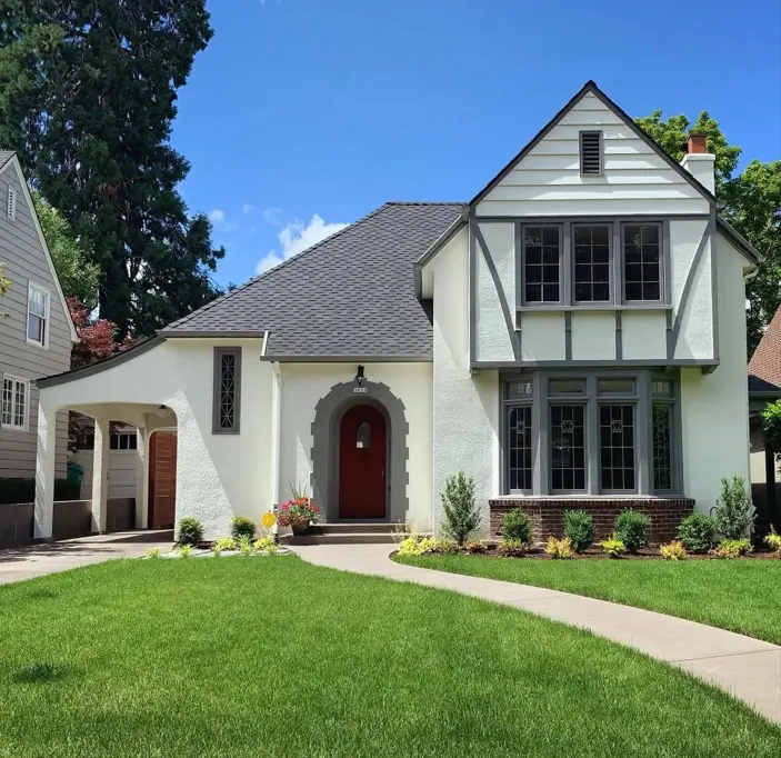 Modern Tudor-style house with crisp white stucco, sophisticated gray trim, and a striking red front door.