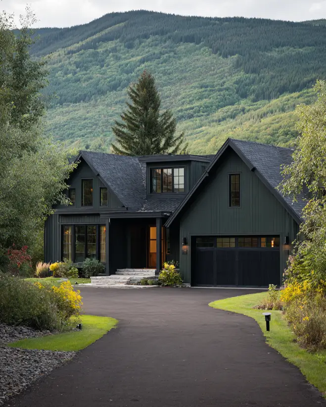 A modern farmhouse painted a deep forest green, with a winding black driveway and a mountain covered in trees.