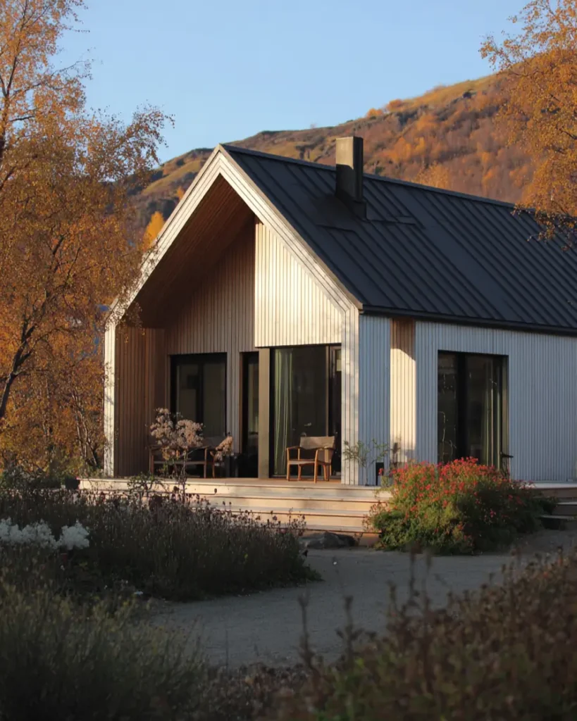 A modern Scandinavian house with light wood siding and a dark roof, set against a backdrop of hills with autumn colors.