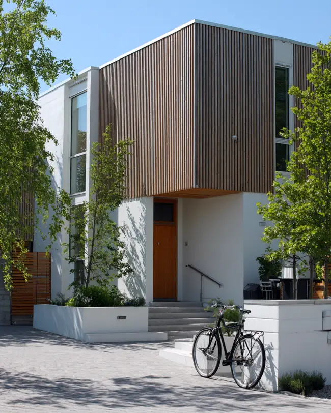 A modern Scandinavian exterior with a white base, vertical wood cladding on the upper level, and a bicycle parked on the driveway.
