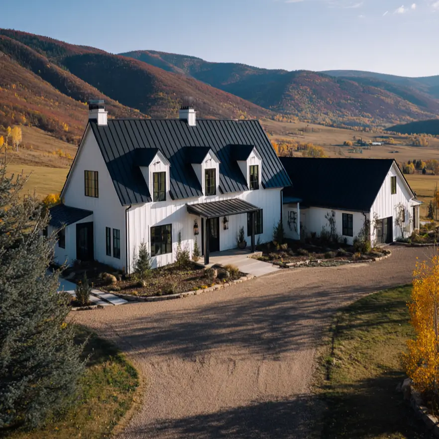 A classic black and white farmhouse exterior with a commanding black metal roof and three dormer windows set against rolling hills.