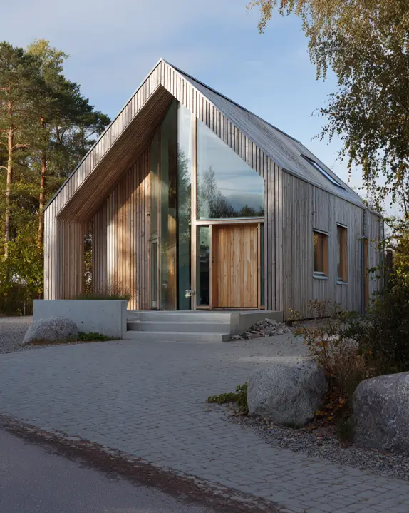 A Scandinavian style home exterior with a striking A-frame roof, light vertical wood siding, and a recessed glass entrance.