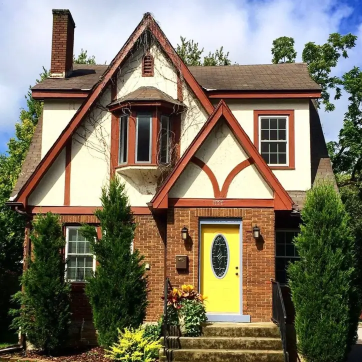 Welcoming small Tudor home with a unique bright yellow front door, warm red trim on the gables, and a classic brick facade.