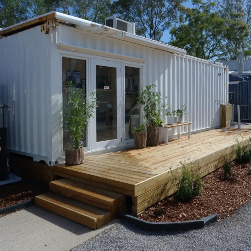 A simple white shipping container converted into a minimalist studio, featuring elegant glass doors that open onto a clean, light-wood deck.