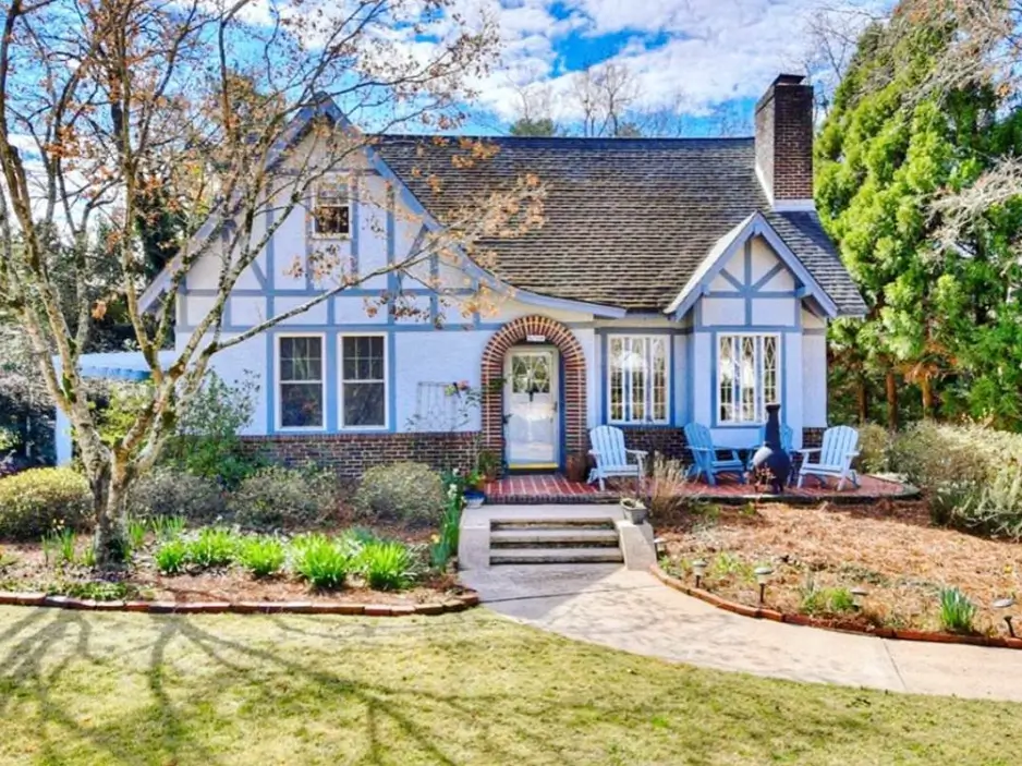 Tudor-style cottage with soft blue timber details that accent the facade and a cozy brick entryway patio.