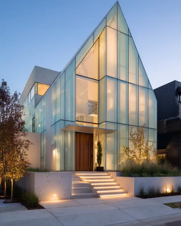 A contemporary A-frame house with a frosted glass facade that glows from within at twilight.