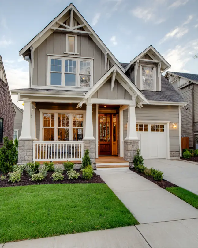 Modern craftsman house with a balanced facade of taupe siding, a welcoming porch with tapered columns on stone piers, and a glass-paneled front door.