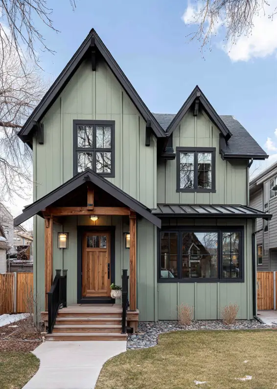 The rustic entryway of a modern sage green house, featuring chunky wood beams that contrast with the sleek black trim.