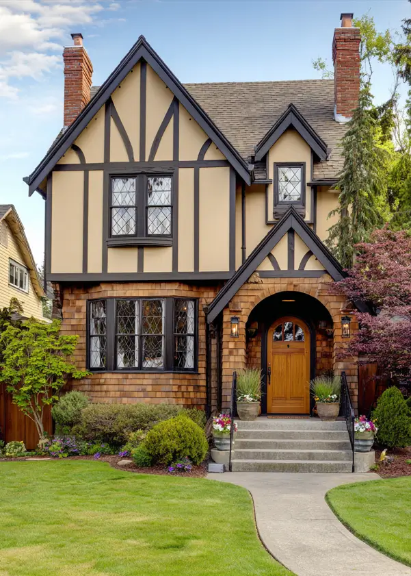 A Tudor-style house exterior featuring warm cedar shingles on the lower level and an arched brick entrance.