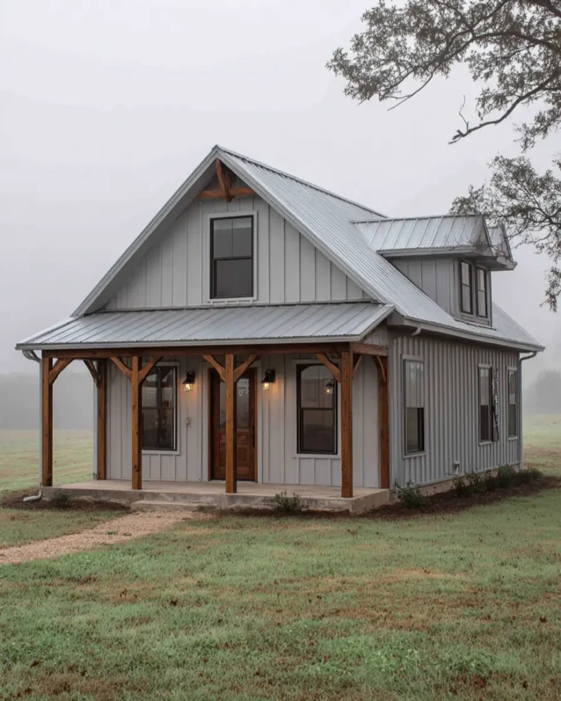 A light gray tiny barndominium house with wooden porch timbers and a complex metal roof on a foggy day.