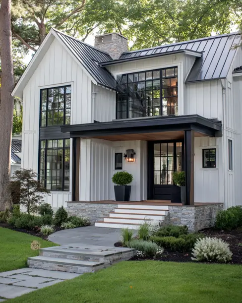 36 Modern Cottage Exterior Ideas to Achieve Timeless Curb Appeal 29 A modern cottage with tall white vertical siding, featuring a dramatic two-story section of black-framed windows and a stone porch foundation.