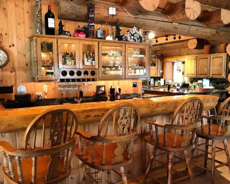 A bright, country-style bar log cabin with traditional captain's chairs and glass-front cabinets.