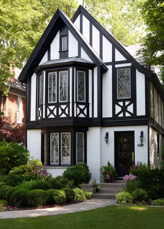 A striking small Tudor-style house with a high-contrast black and white exterior, highlighting a projecting bay window with diamond panes.