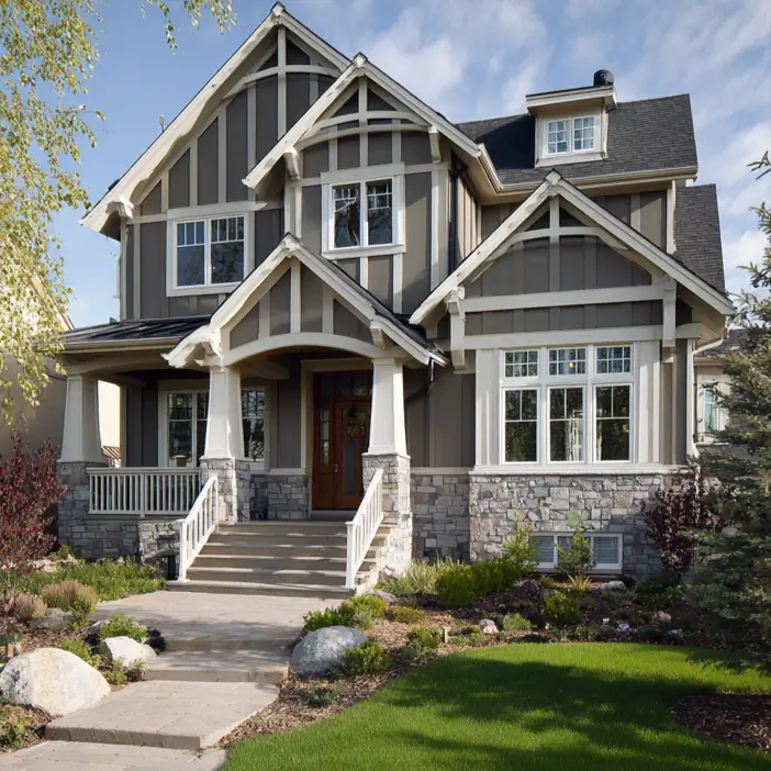 Modern craftsman style house with taupe vertical siding and detailed white trim in the gables, featuring a porch with columns on stone piers.