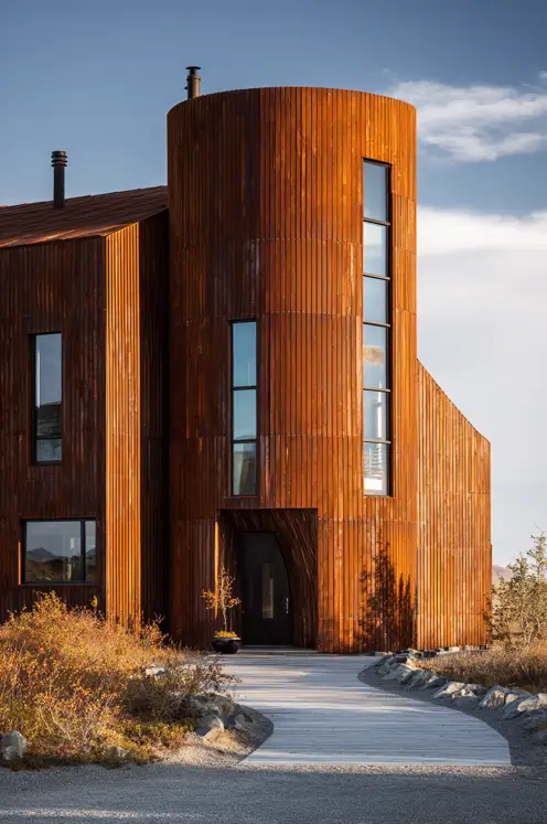 A striking, rust-colored grain silo house featuring tall, vertical windows that emphasize its height against a blue sky.