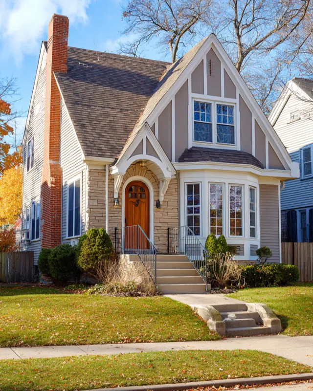 A Tudor-style house that mixes stone accents and light-colored siding, with a prominent bay window.