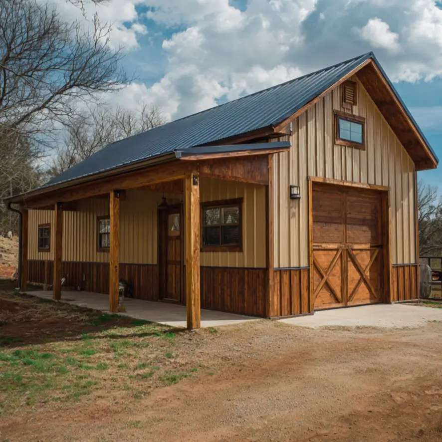 A barndominium home with tan siding, wood wainscoting, and a large wooden garage door under a partly cloudy sky.