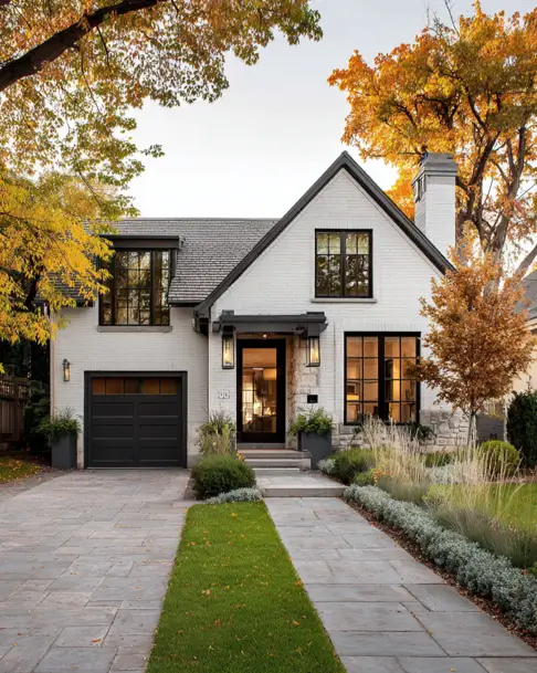 36 Modern Cottage Exterior Ideas to Achieve Timeless Curb Appeal 6 A modern cottage with a painted white brick exterior, black-framed windows, and a driveway with a unique grass strip between stone pavers.