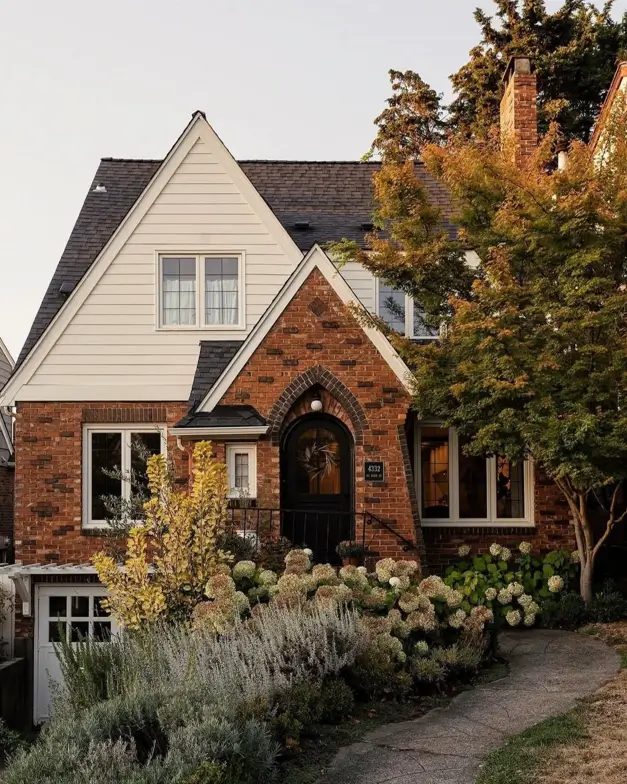 Elegant small Tudor-style house defined by a prominent brick archway over the front door and clean white siding on the upper level.