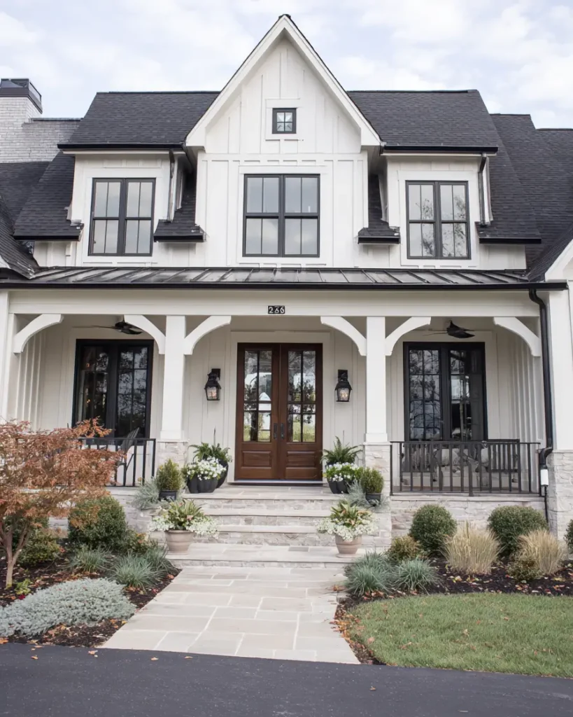 A white and black modern farmhouse featuring a welcoming front porch with a warm wooden door and bold black garage doors.