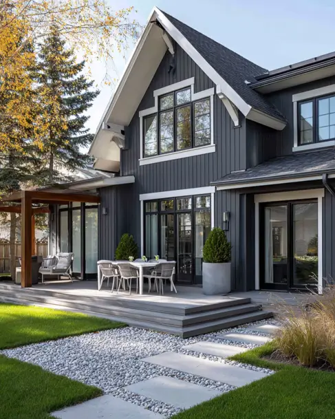 36 Modern Cottage Exterior Ideas to Achieve Timeless Curb Appeal 37 The rear exterior of a modern cottage with dark gray siding, showing a large multi-level deck with an outdoor dining set and a pergola.