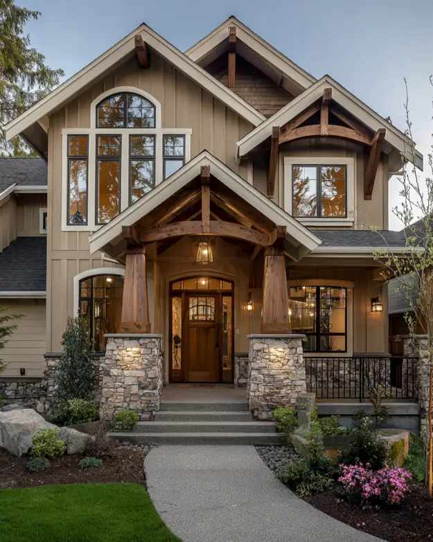 Modern craftsman style house entrance featuring a large arched window above the door, heavy timber columns on stone piers, and tan siding.