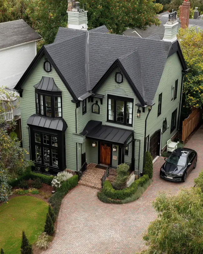 An aerial perspective of a grand sage green house with an impressive herringbone-patterned paver brick driveway.