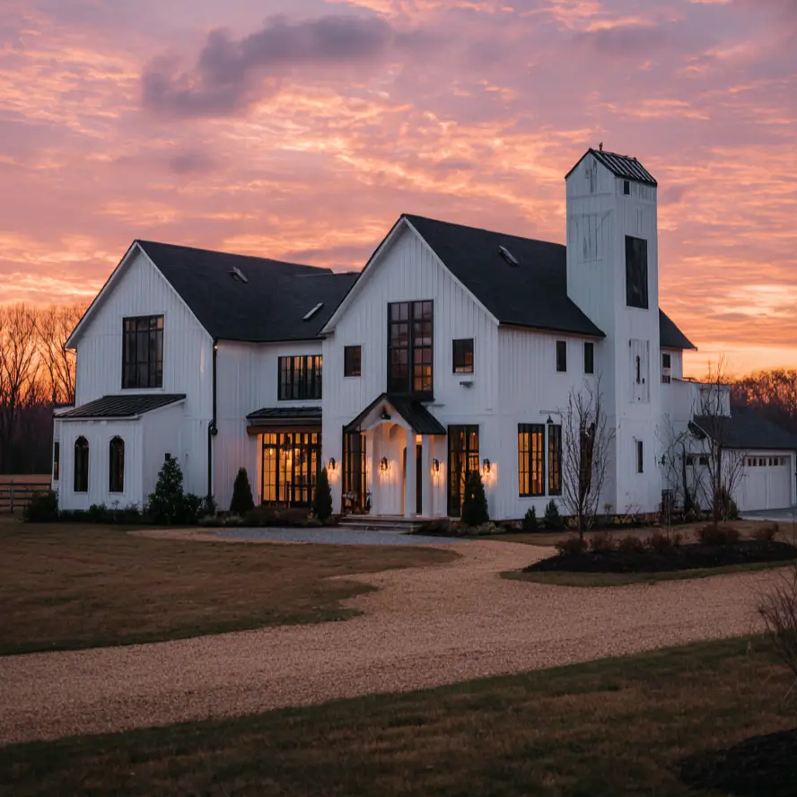 A dramatic white and black modern farmhouse with a unique silo tower against a colorful sunset sky.