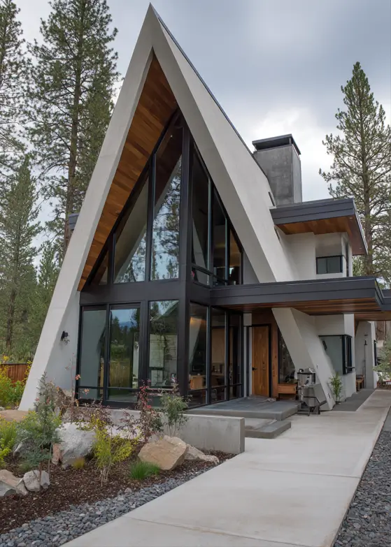 A modern A-frame house with a sculptural concrete exterior, wood accents, and an asymmetrical design among pine trees.
