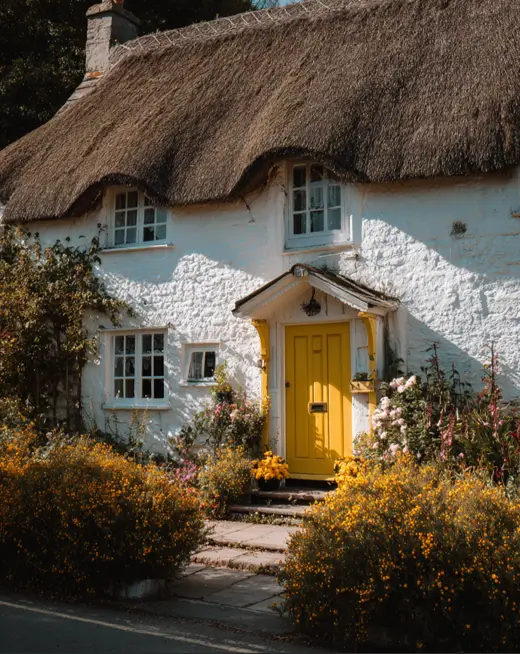 A whitewashed english cottage with a thatched roof, featuring a vibrant, sunny yellow front door that creates a cheerful focal point.