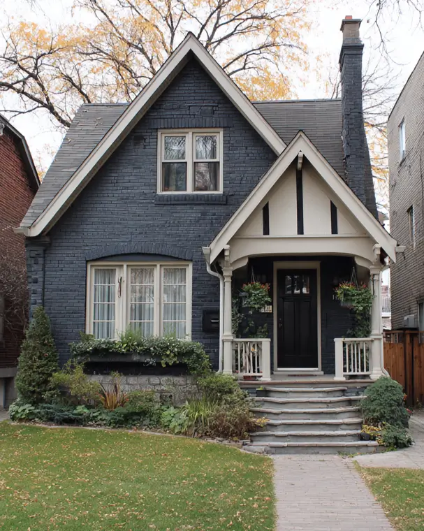 A moody small modern Tudor home with a dark charcoal painted brick exterior and a contrasting, brightly lit cream-colored entryway.