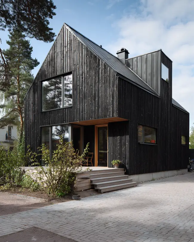 A Scandinavian style home exterior featuring textured black vertical siding and smooth metal roof details, with a simple wooden stoop.