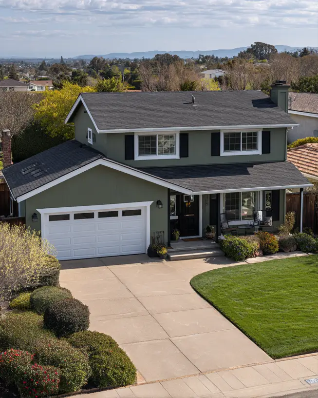 The classic facade of a two-story sage green house, where bold black shutters provide a timeless contrast against the siding.