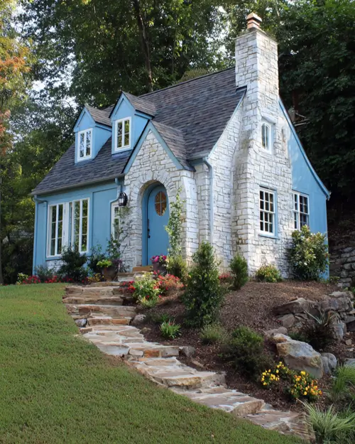 A small blue cottage with a white stone arched entryway and chimney, showcasing a storybook exterior design.