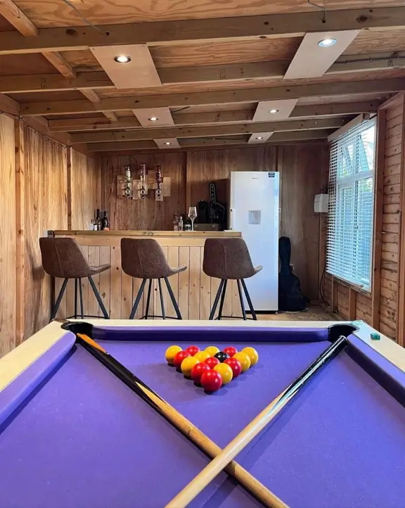 A simple bar log cabin designed as a game room, with a purple pool table in the foreground.