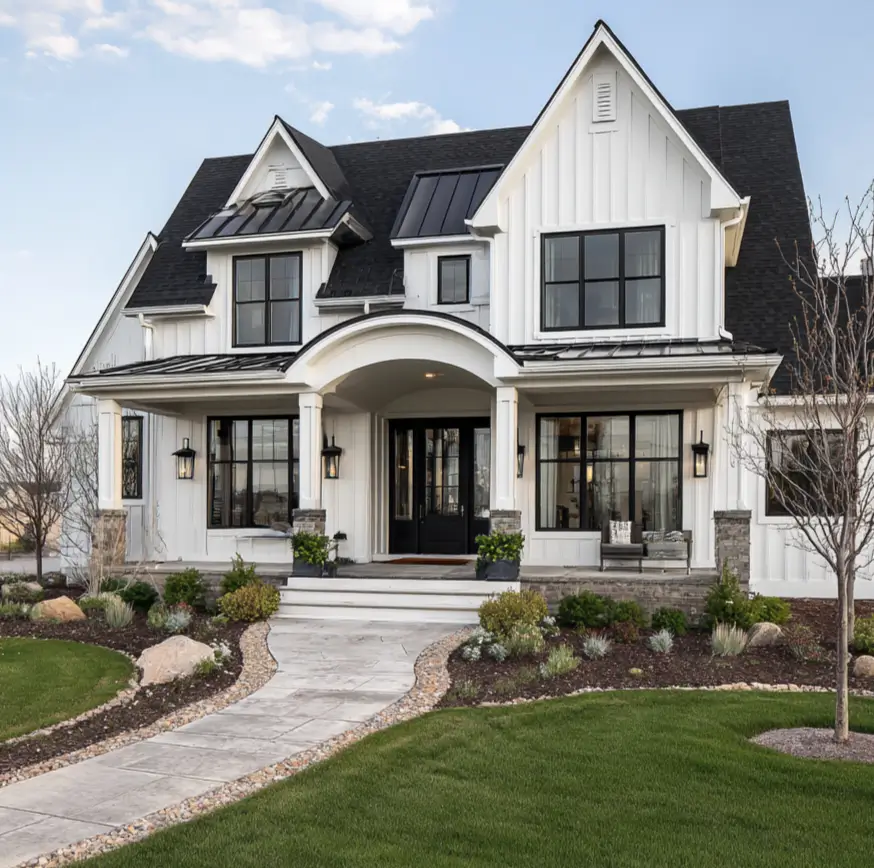 A white modern farmhouse with an elegant arched portico and natural stone bases on the porch columns.