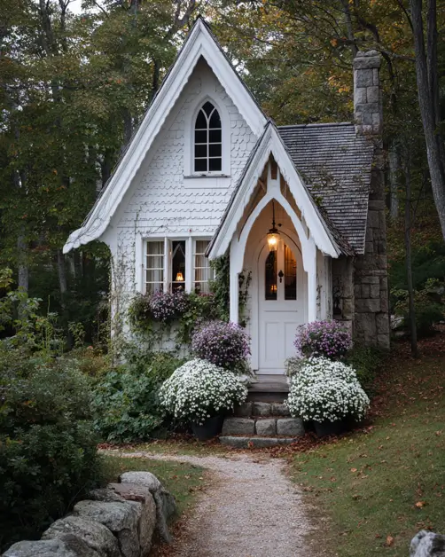 A small white storybook cottage with a steep roof and an arched Gothic window, showcasing an exterior design for small houses.