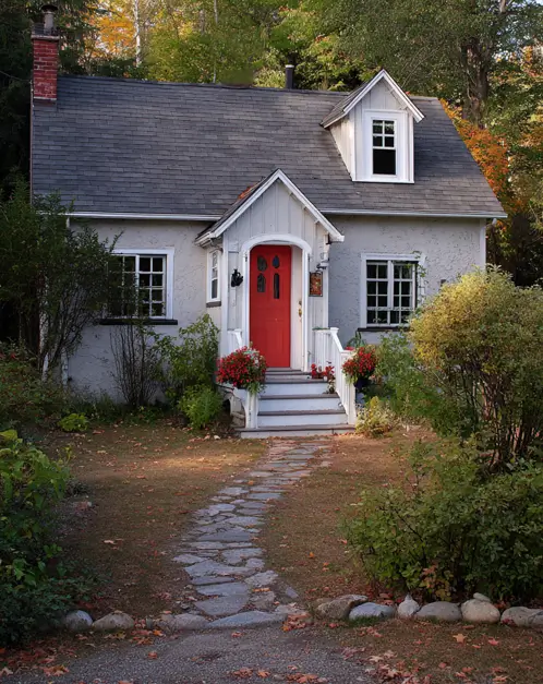 A small gray cottage with a bright red front door and a stone path, presenting a classic small house exterior idea.