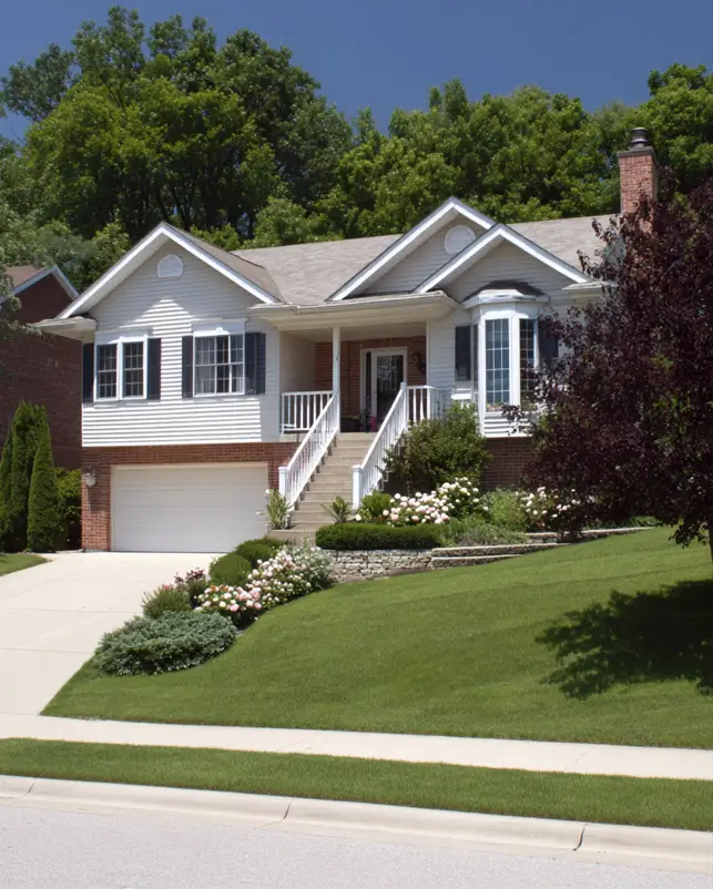 A split-level suburban house exterior on a sloped lot, using tiered landscaping and an elevated main entrance to work with the natural grade of the yard.