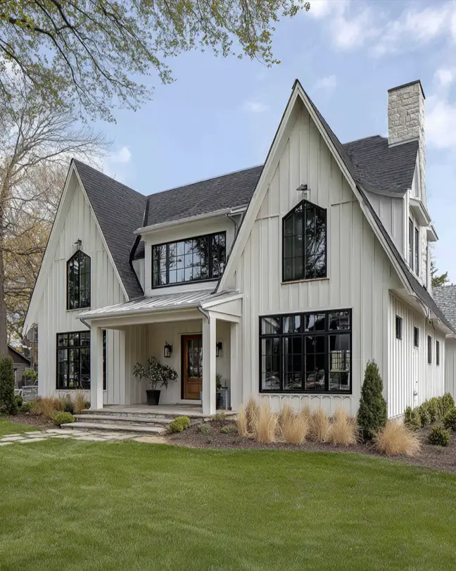 A large white and black modern farmhouse featuring elegant arched black-framed windows and a stone chimney.