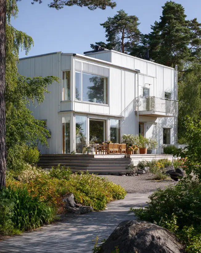 A multi-level modern Scandinavian exterior in white with a wooden deck and large windows, surrounded by trees.