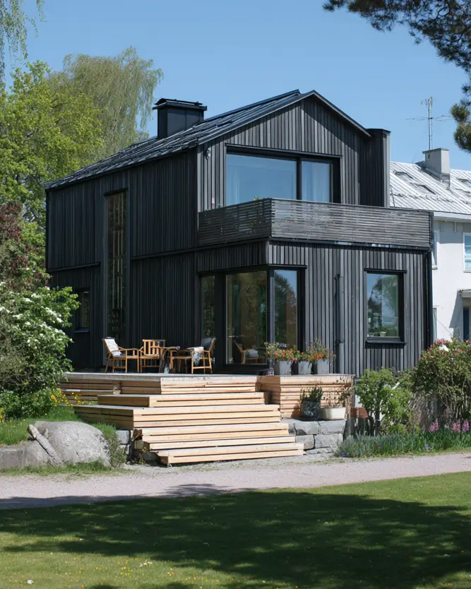 A dark modern Scandinavian house exterior with a projecting balcony and a wide, natural wood deck.