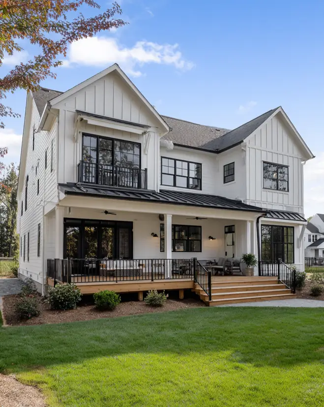 The rear exterior of a white and black modern farmhouse showing a large covered wood deck and a second-story balcony.